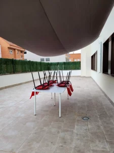 Terraza exterior con mesa, sillas rojas y toldo